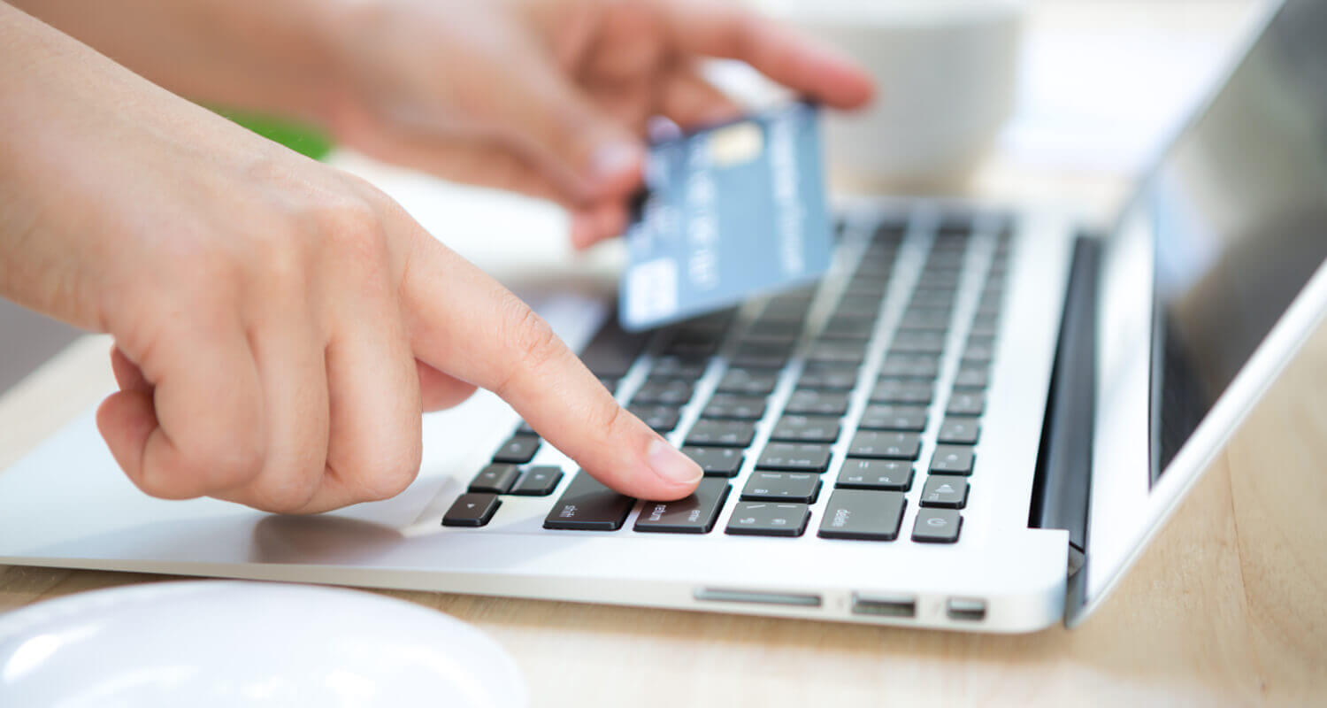 Pessoa digitando em um notebook com o cartão na outra mão, realizando uma compra Confira os melhores sites para você comprar um iPhone!