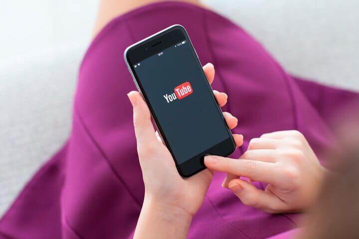 mãos segurando um celular na vertical com ícone do youtube baixar-filme-pelo-celular