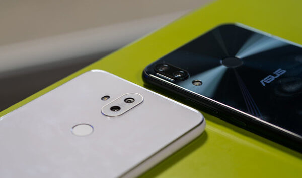 Zenfone 5 Zenfone 5 em duas cores, preto e branco. Ambos estão com a parte traseira para cima, sobre uma mesa verde.