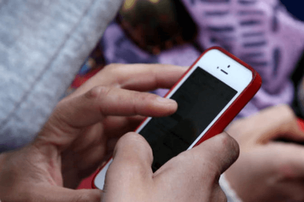 Pessoa utilizando um iPhone branco com capinha vermelha, embora a tela do aparelho esteja escura. 