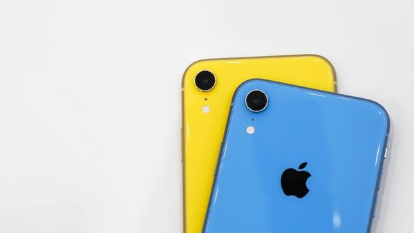 Dois aparelhos iPhone XR com sua parte traseira em destaque. O da frente é azul e o de trás é amarelo, e ambos estão sobre uma superfície branca.