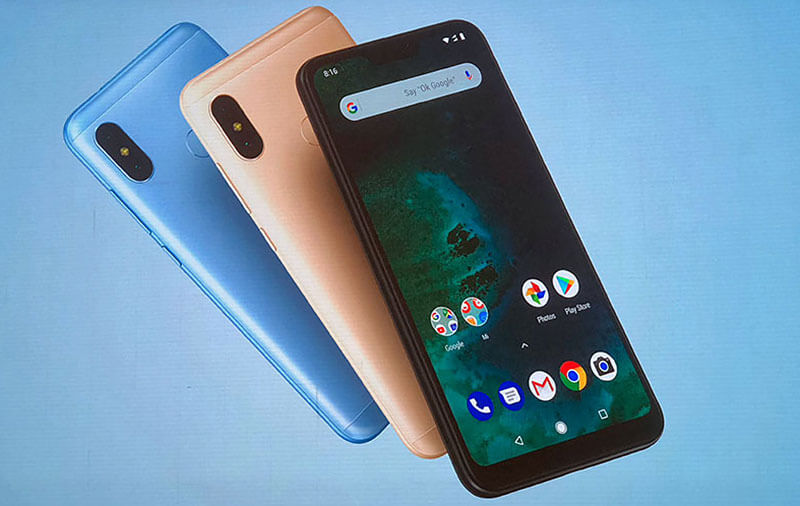 Foto com 3 aparelhos Xiaomi Mi A2 Lite sobre um fundo azul. O aparelho que aparece em maior destaque está de frente, tem a cor preta e está com a tela ligada, enquanto os outros dois estão dispostos com a parte traseira para cima, atrás do primeiro aparelho, nas cores rose gold e azul, respectivamente.