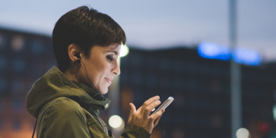 Jovem mulher utilizando o celular em rua movimentada