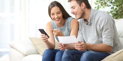 Homem e mulher sentados no sofá olhando para tela de um celular